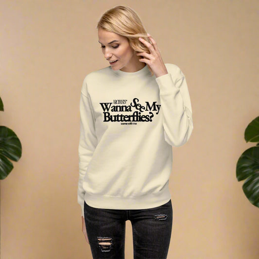Woman wearing a beige wanna see my butterflies sweatshirt with text on a white background